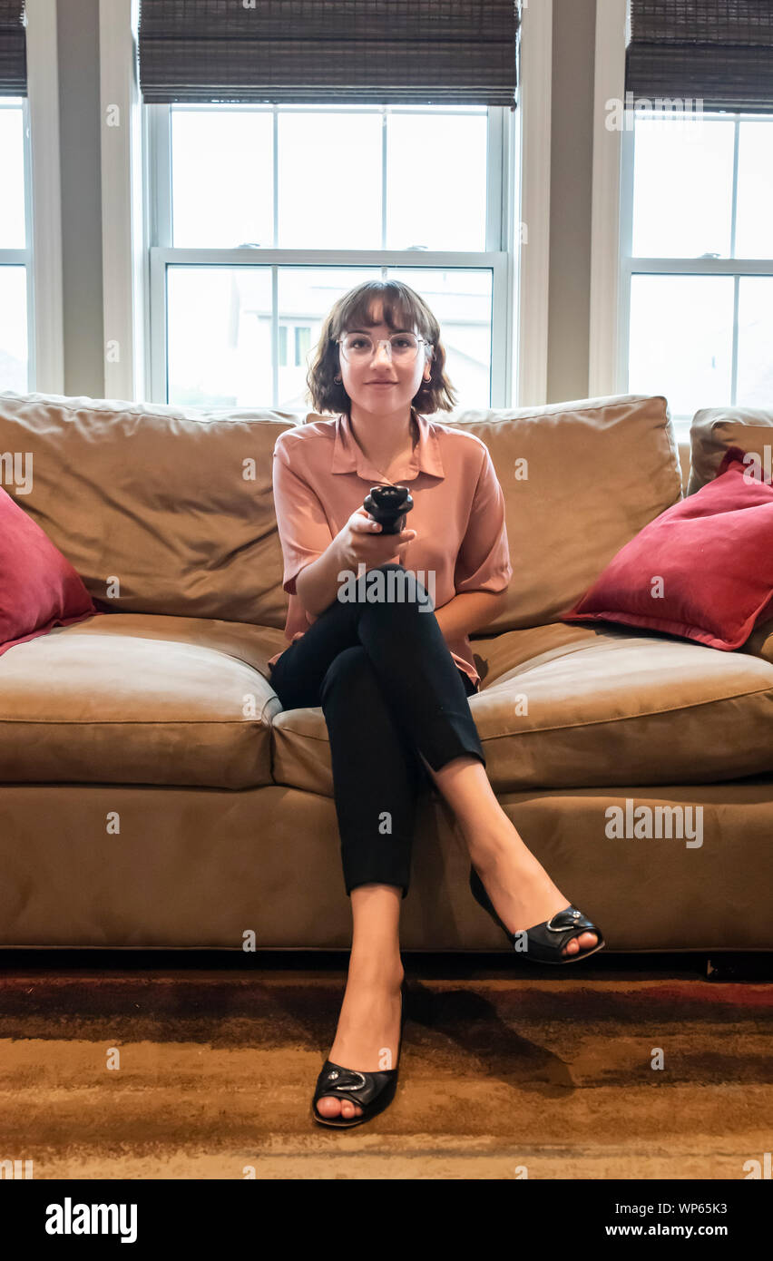 Young woman sitting on a couch in business attire watching television. Stock Photo