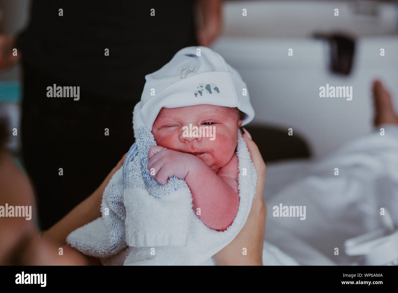 Authentic birth images, newborn baby being help by mother. Wearing a little white hat Stock Photo