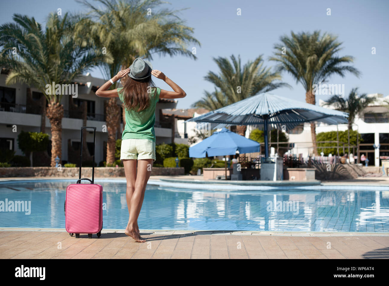 Travel, summer holidays and vacation concept - Beautiful woman walking near hotel pool area with pink suitcase Stock Photo