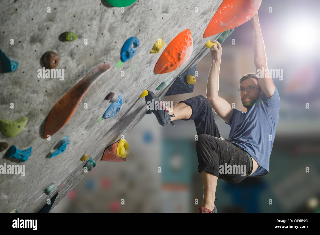 young active sport man with beard and glasses climbing on gym wall