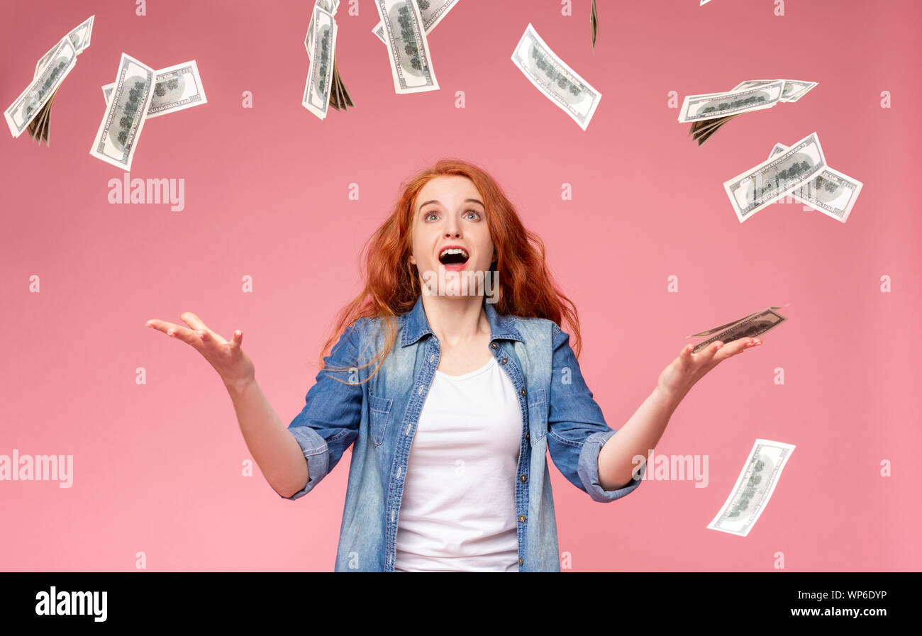 Excited redhead girl standing under money shower Stock Photo