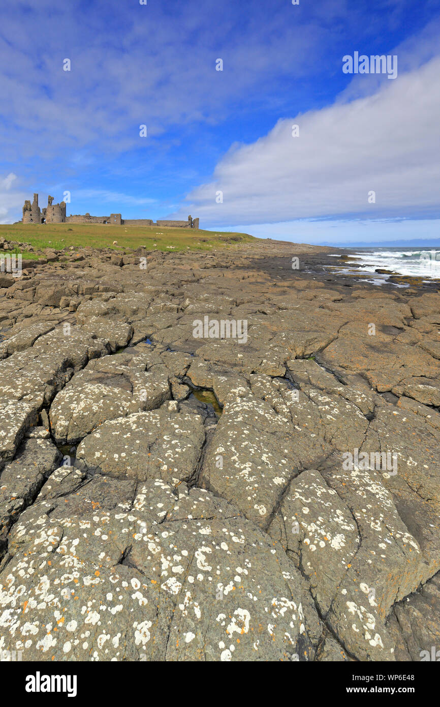 Dunstanburgh Castle from the rocky shoreline on the Northumberland Coast Path near Craster, Northumberland, England, UK. Stock Photo