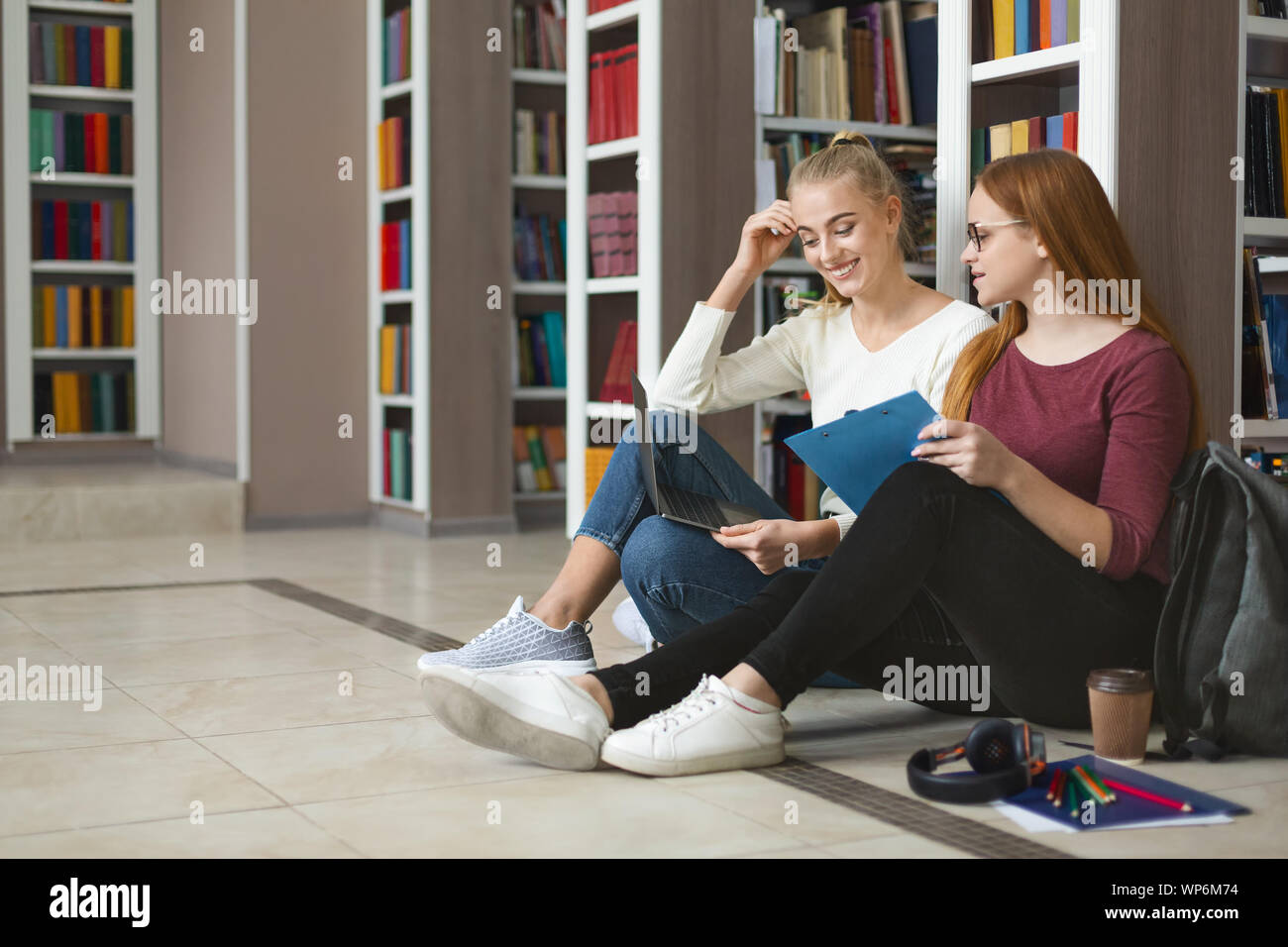 Pretty teenage girlfriends studying on floor in library Stock Photo