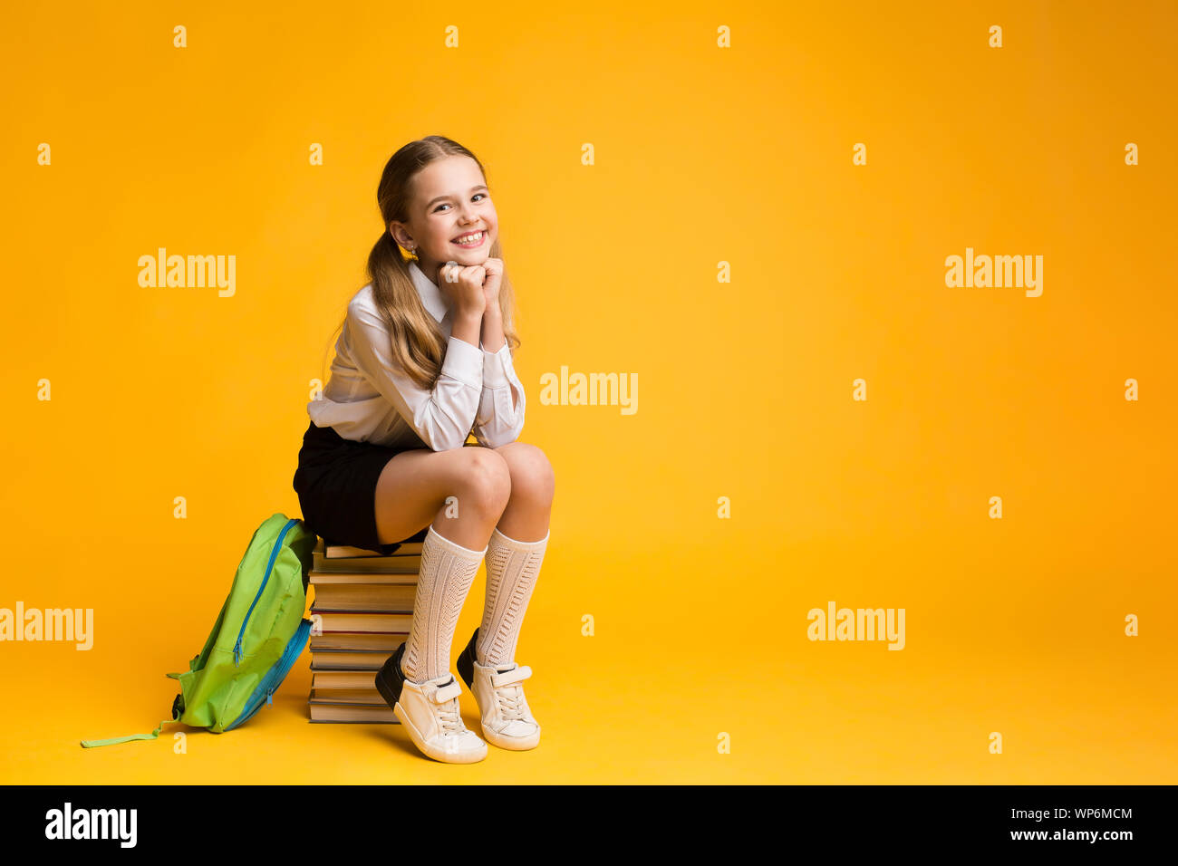 Cute School Girl Sitting On Book Stack On Yellow Background Stock Photo ...