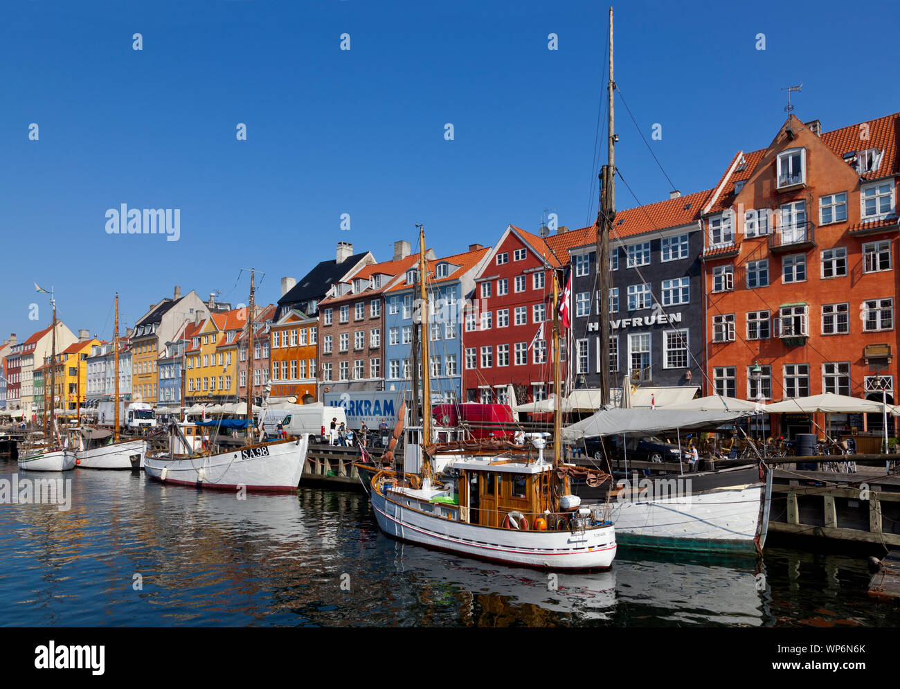 Beautiful old vessels and sailing ships in popular Nyhavn canal. Brightly coloured houses. Restaurants and bars crowded with tourists and visitors. Stock Photo