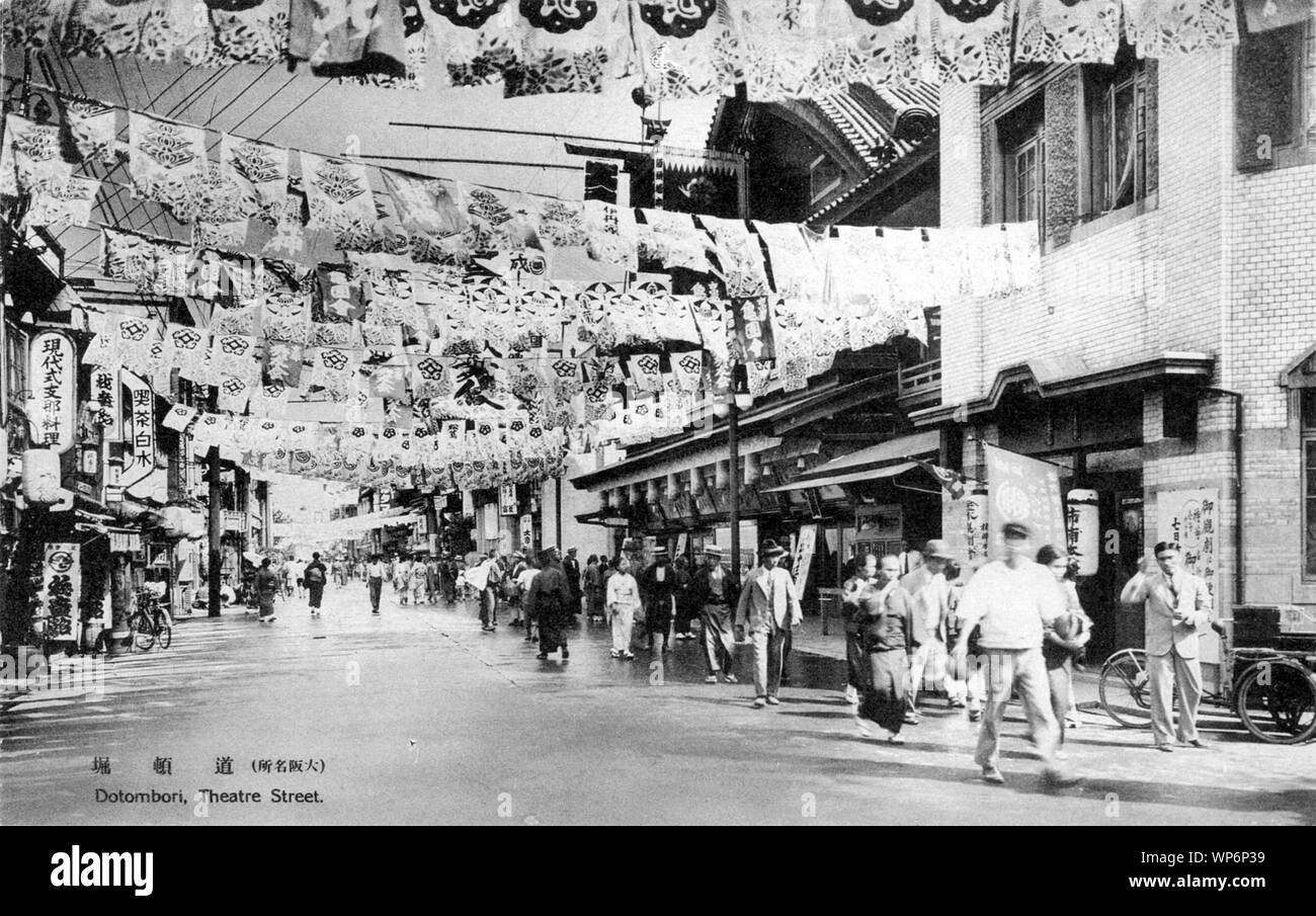 [ 1930s Japan - Dotonbori Entertainment District in Osaka ] —   Flags advertise businesses on Dotonbori, Osaka.  The crowded and lively street, designated as the theater and entertainment district in 1621, was filled with teahouses (shibai-jaya), restaurants and theaters. During the Meiji Period, the five main theaters were called the Dotonbori Goza (道頓堀五座).  During the US firebombing of Osaka in 1945 (Showa 20), these theaters were destroyed or badly damaged.  20th century vintage postcard. Stock Photo