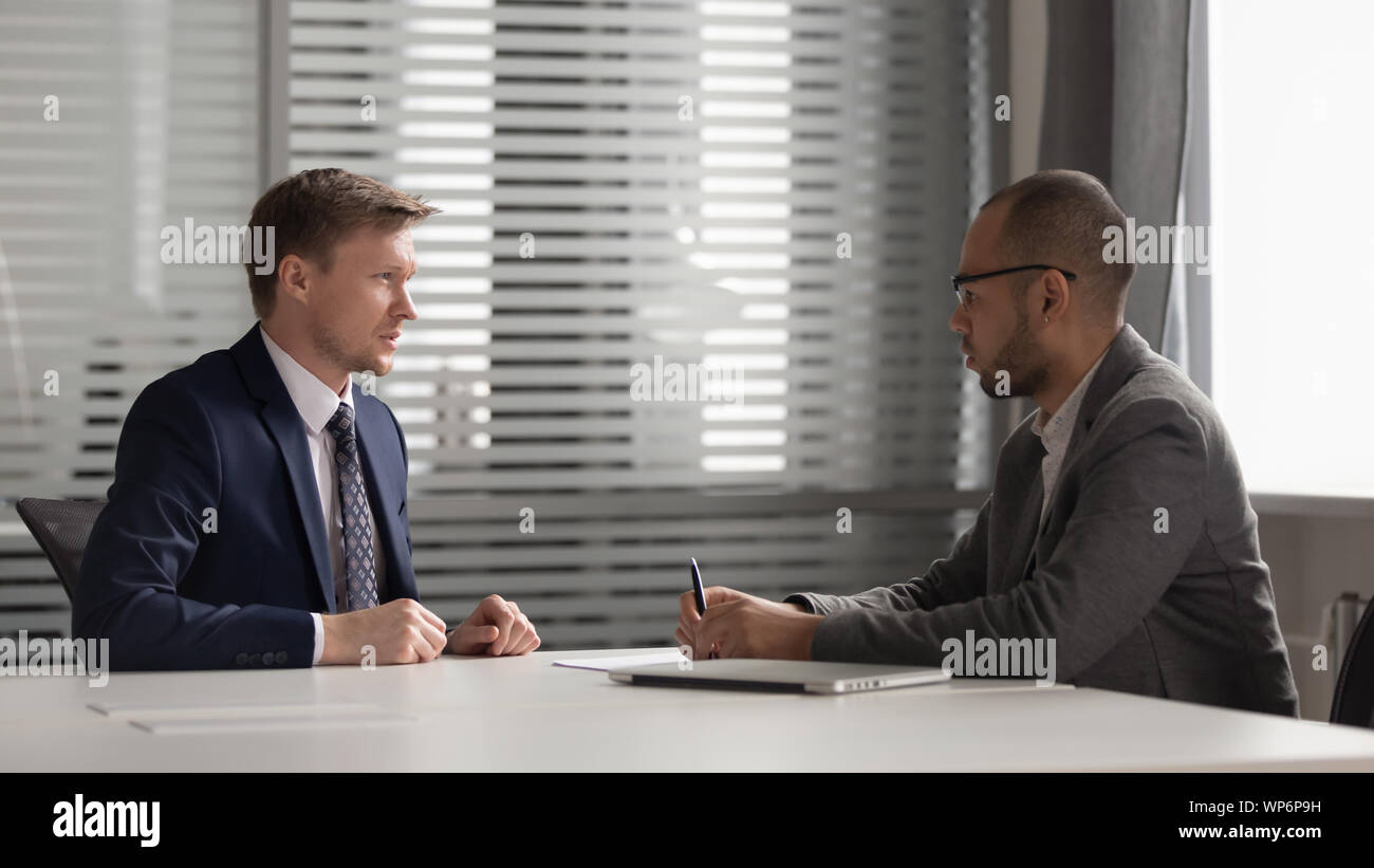 Two multiracial focused male partners discussing company development strategy. Stock Photo