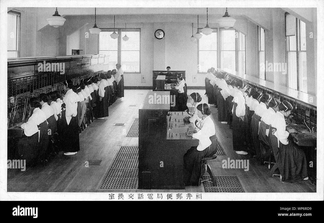 [ 1920s Japan - Japanese Telephone Switching Center ] —   Dozens of young women in uniform work at switchboards at a telephone switching center of Fukui Yubinkyoku (Post Office).  Fukui Yubinkyoku was established on April 8, 1872 (Meiji 5).  Japan imported its first telephone in 1877 (Meiji 10). Female telephone operators were called Hello Girls (ハローガール).  20th century vintage postcard. Stock Photo