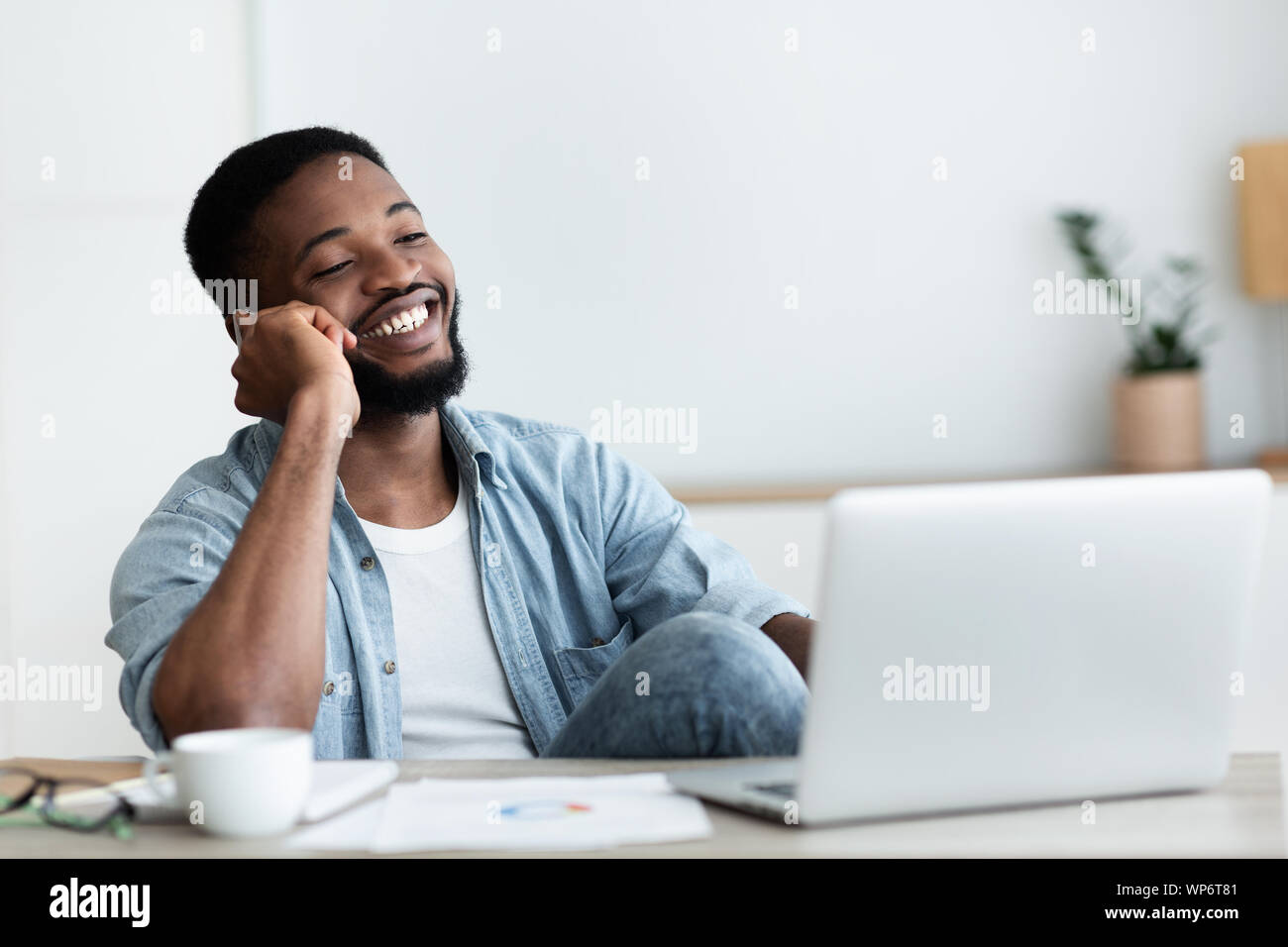 African guy talking on phone, working on laptop in office Stock Photo