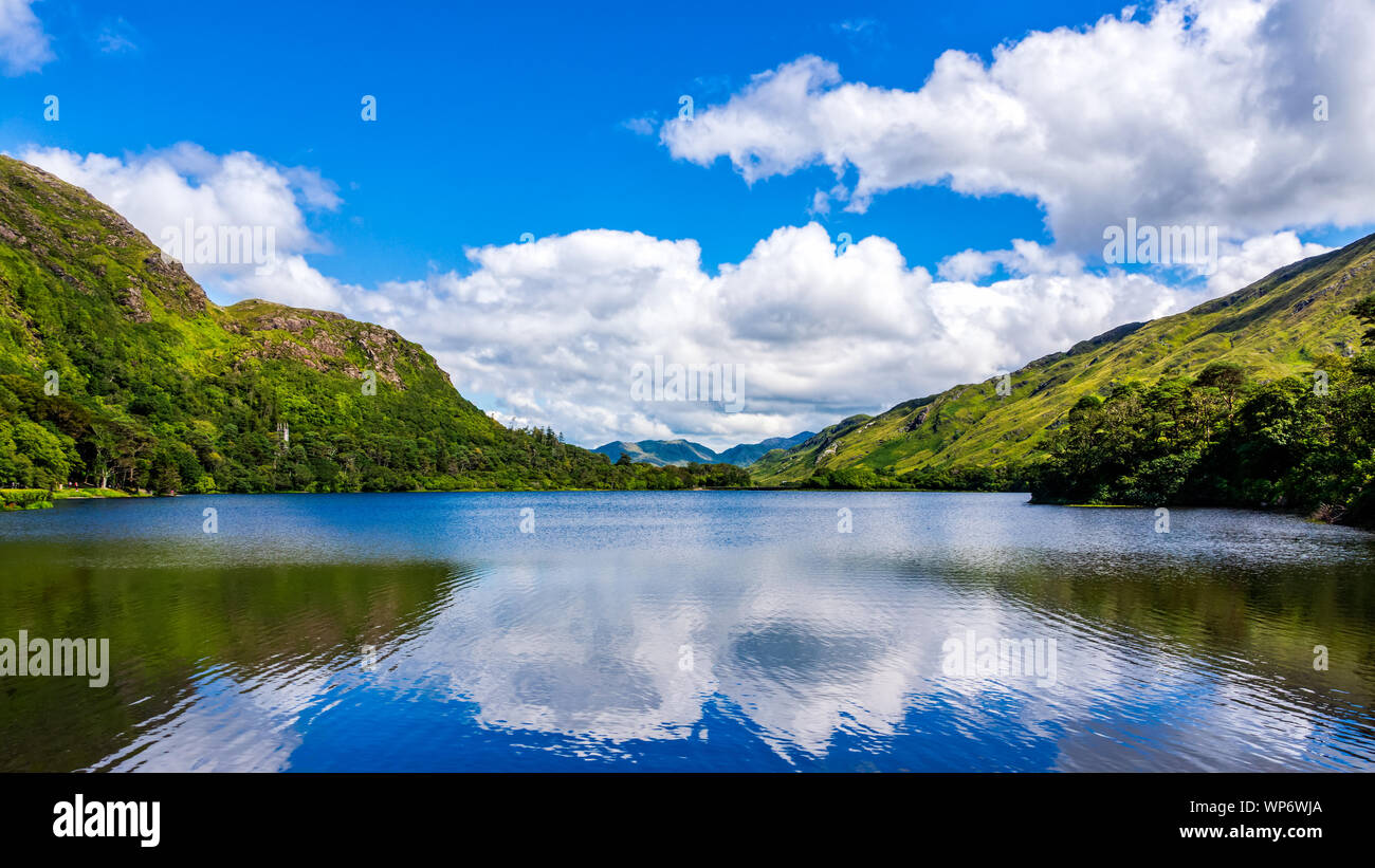 Beautiful shot of a tranquil lake and mountain with puffy clouds reflected in water. Scenic green meadows and hills of Connemara, Ireland Stock Photo