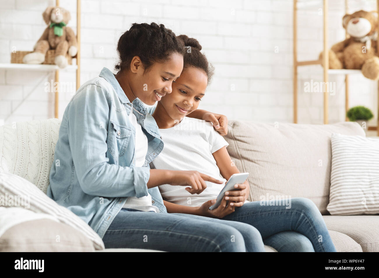 Two cute sisters using phone on sofa at home Stock Photo - Alamy