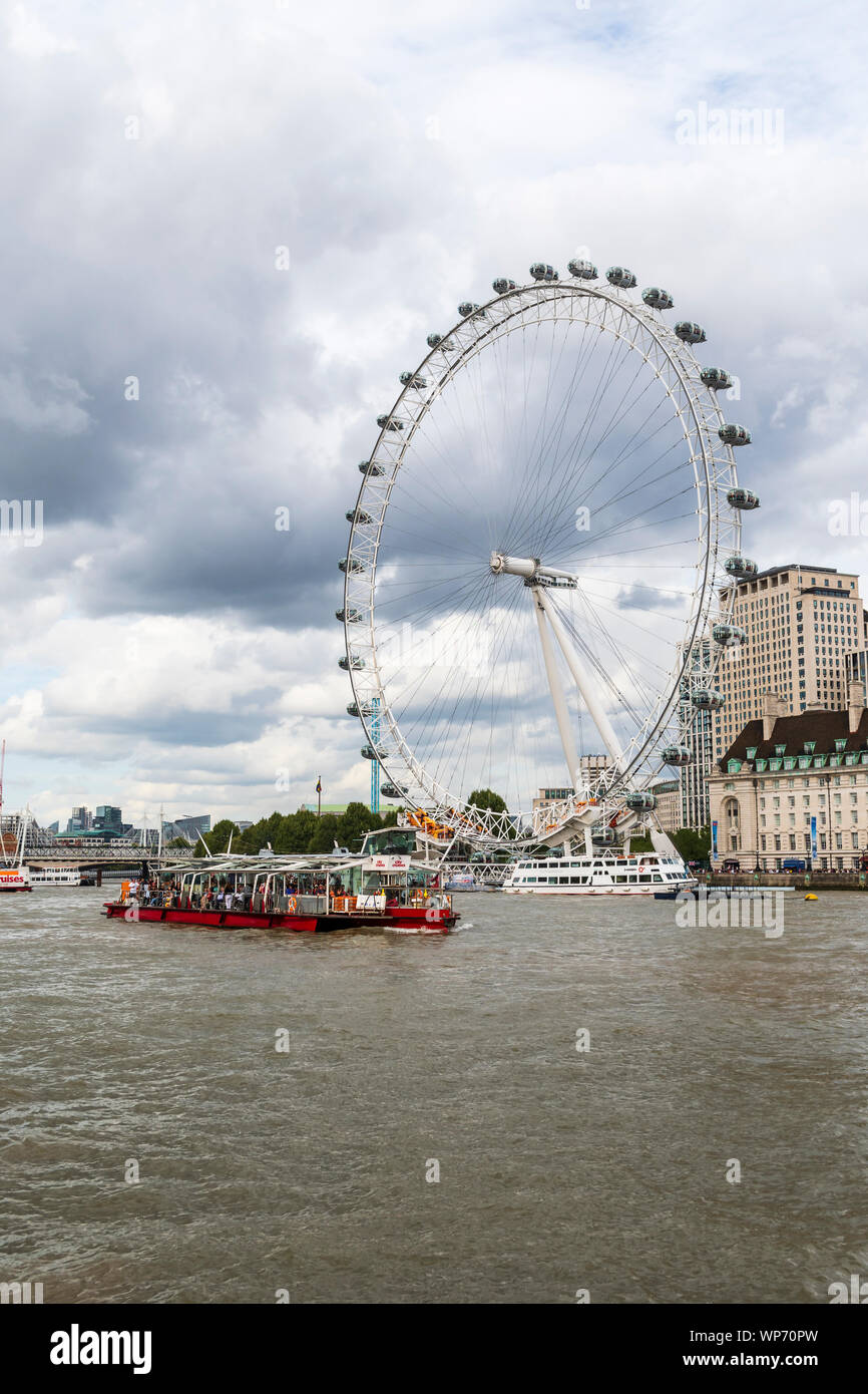 A sightseeing boat cruises in front of the London Eye Stock Photo