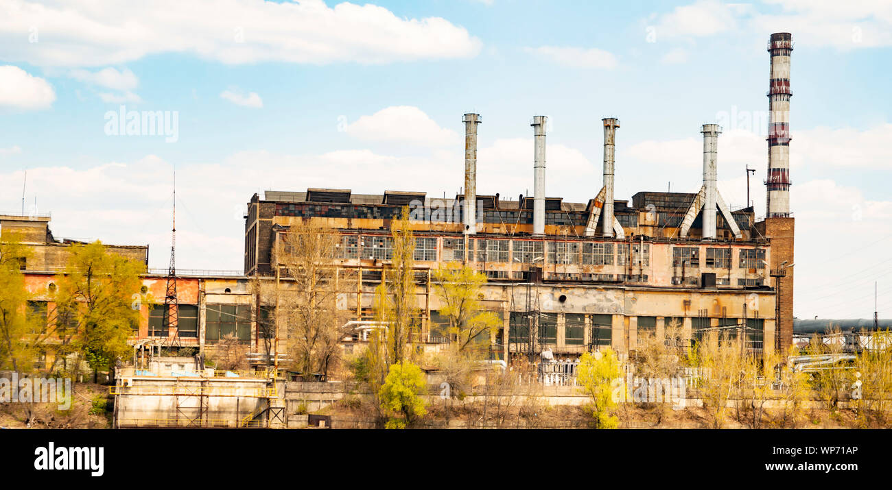 Old industrial factory with pipes on the river bank on a sunny day ...