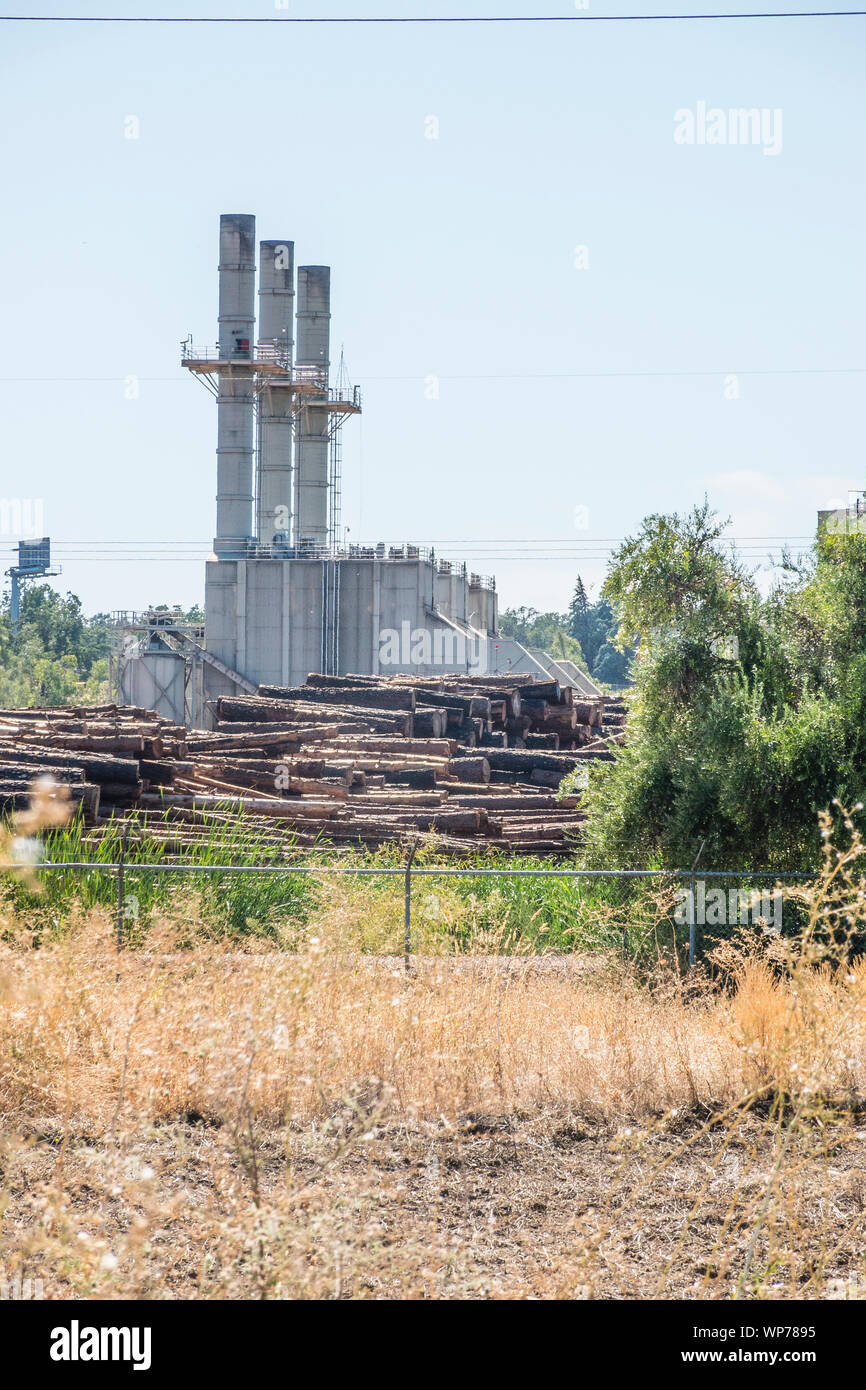 A large lumber mill in Southern Oregon with three large smoke stacks and plles of tree trunks