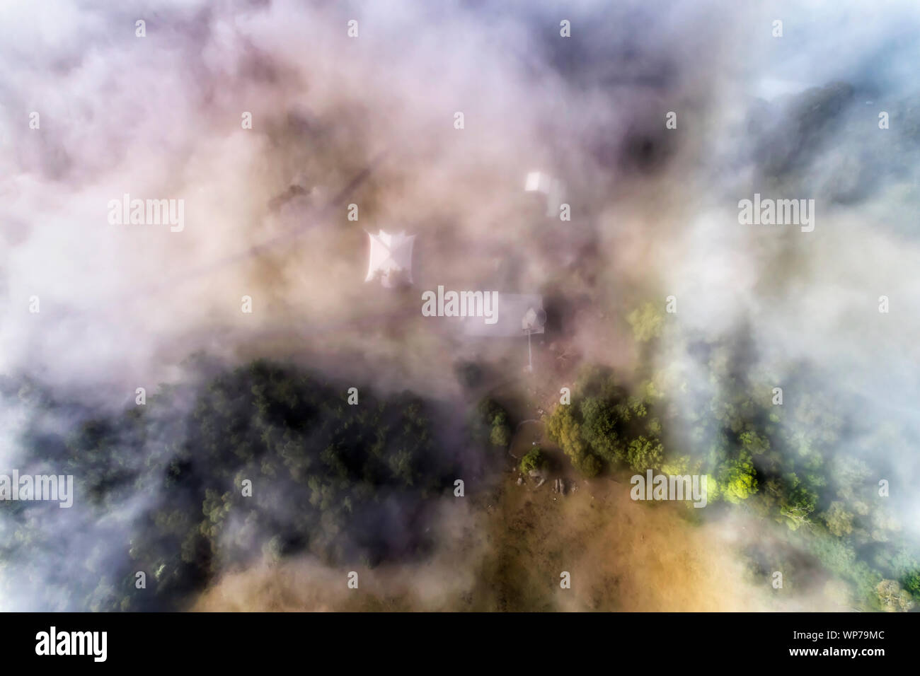 THick white fog covering remote agricultural farm in Kangaroo Valley of Australia. Aerial  top down view over gum-trees and paddocks around farm house Stock Photo