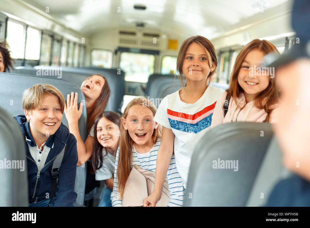 Classmates going to school by bus sitting inside talking to driver cheerful Stock Photo
