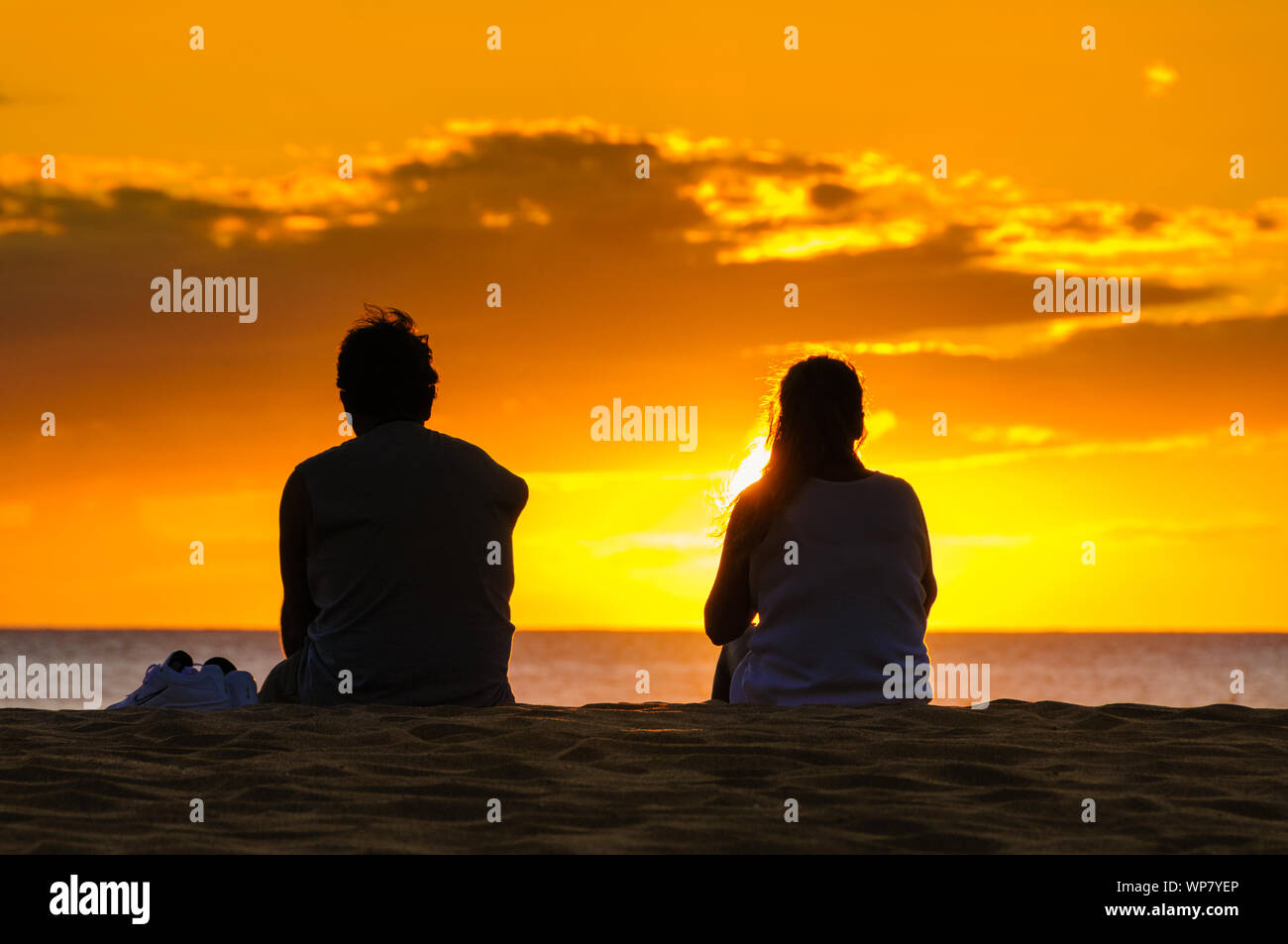 Silhouette of a couple watching a colorful sunset on a beach in Maui ...