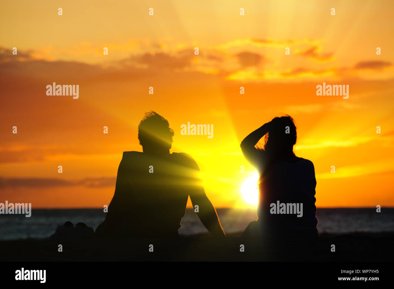 Silhouette of a couple watching a colorful sunset on a beach in Maui ...