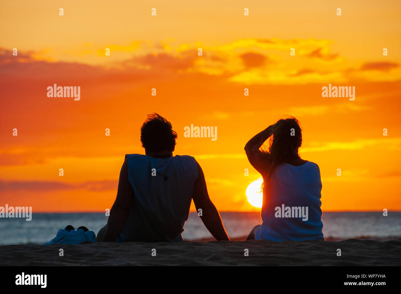 Silhouette of a couple watching a colorful sunset on a beach in Maui ...
