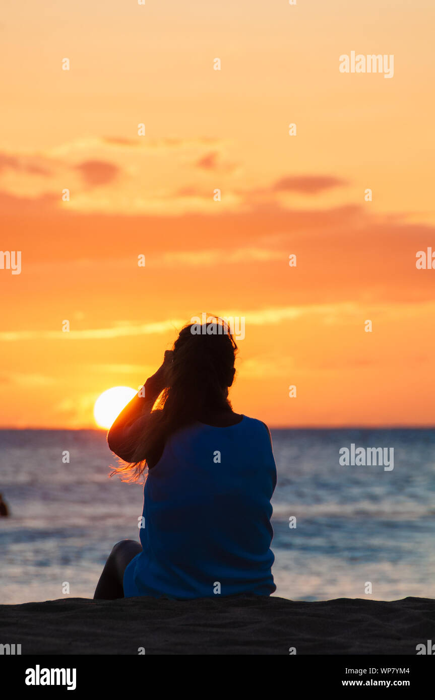 Silhouette of a woman watching a colorful sunset on a beach in Maui ...