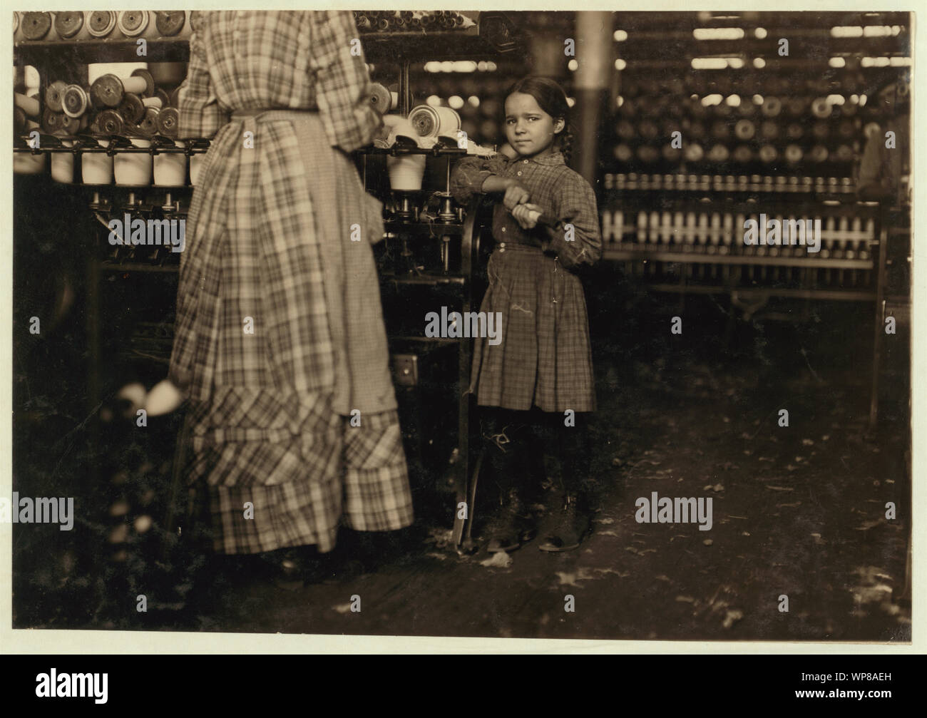 Little Fannie, 7 years old, 48 inches high, helps sister in Elk Mills. Her sister (in photo) said, Yes, she he'ps me right smart. Not all day but all she can. Yes, she started with me at six this mornin'. These two belong to a family of 19 children. Stock Photo