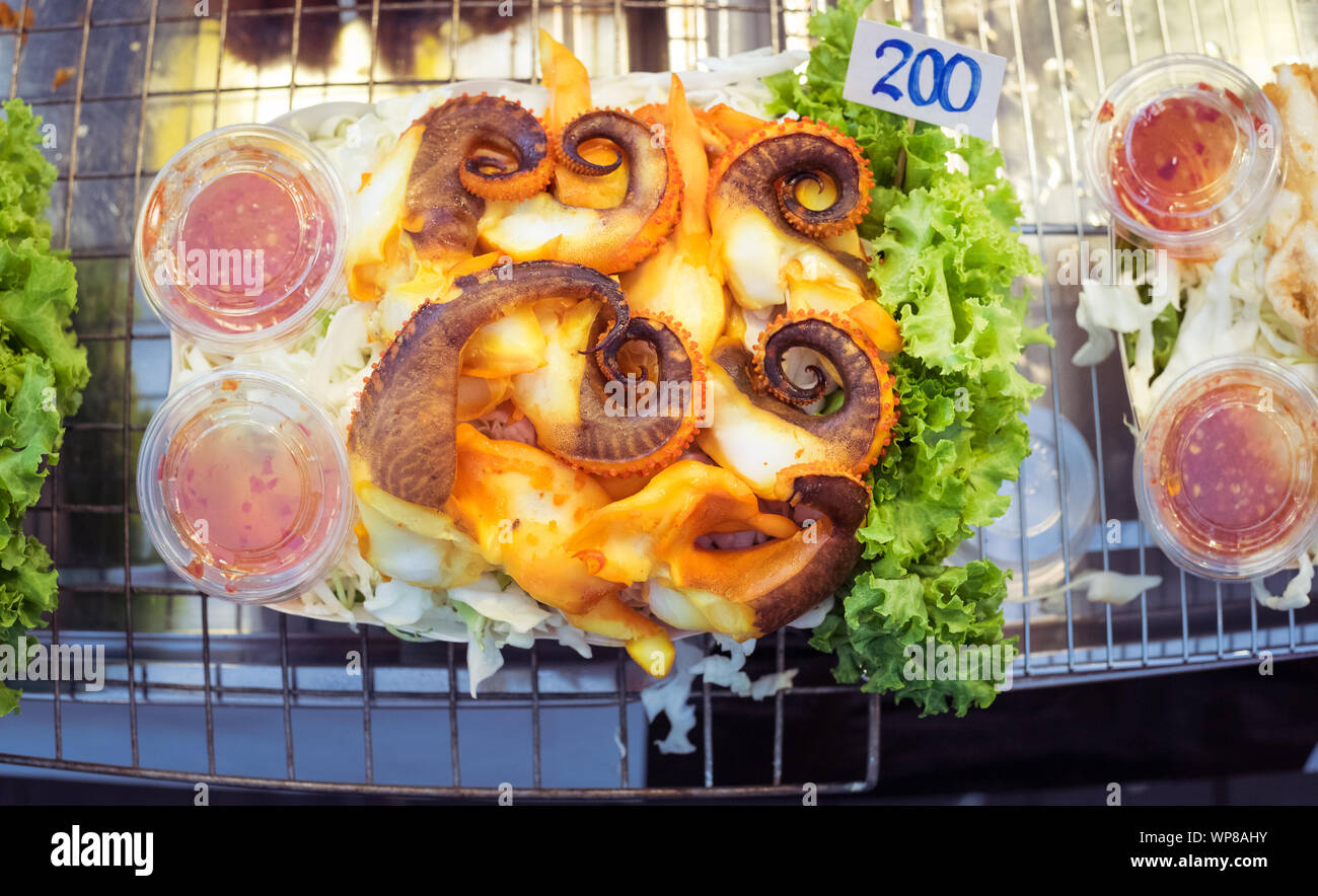 Grilled octopus with chili sauce, chopped cabbage, and lettuce. At a street food market at Asiatique The Riverfront in Bangkok, Thailand. Stock Photo