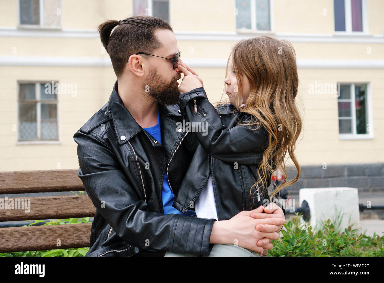 Fashionable stylish family for a walk. Happiness to be a parent. Charming little daughter is sitting on her father's lap. Time of prank. Confidential Stock Photo