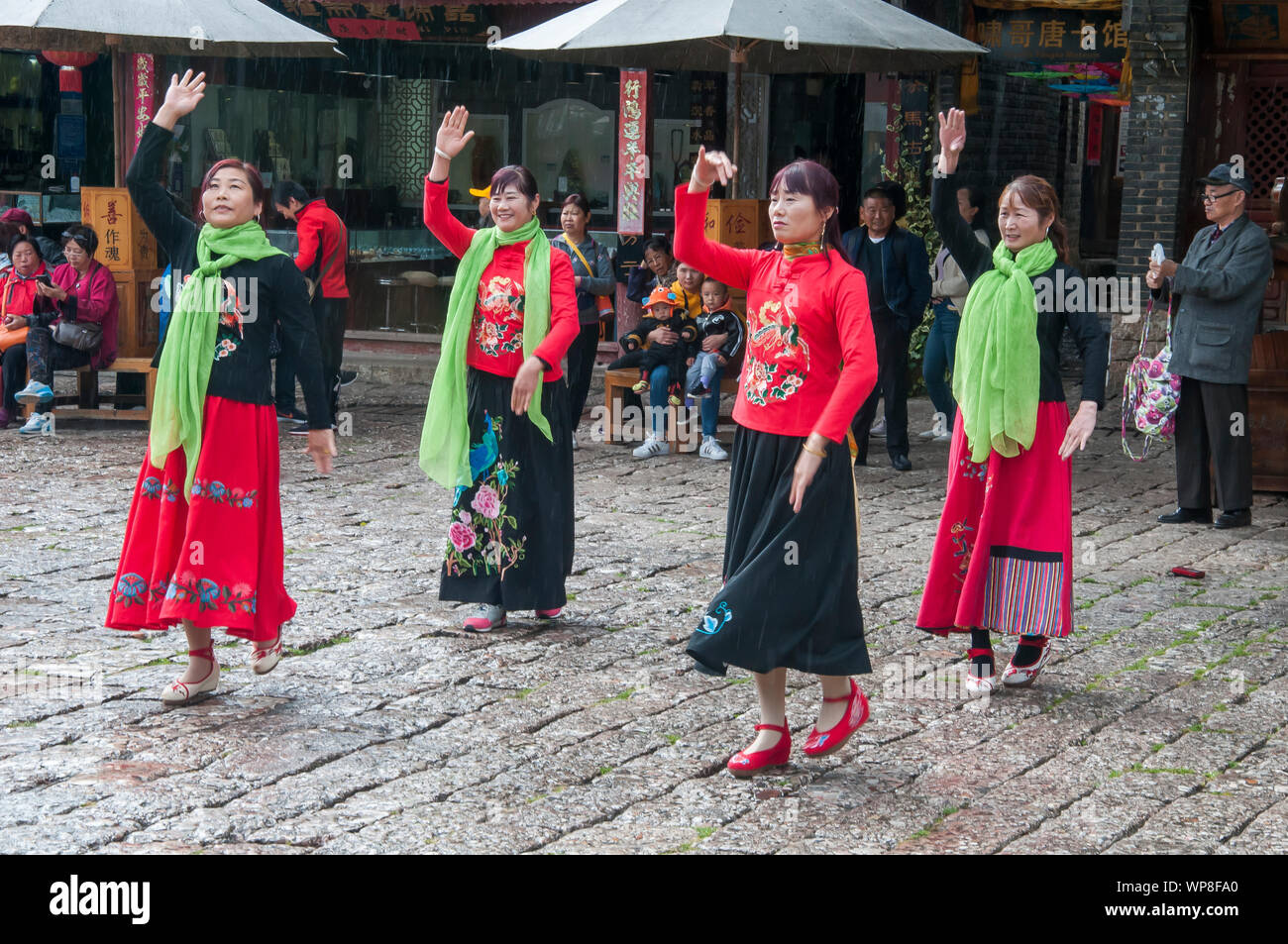 Female folk dancers perform in a town square in the Old Quarter of Lijiang, Yunnan, China Stock Photo