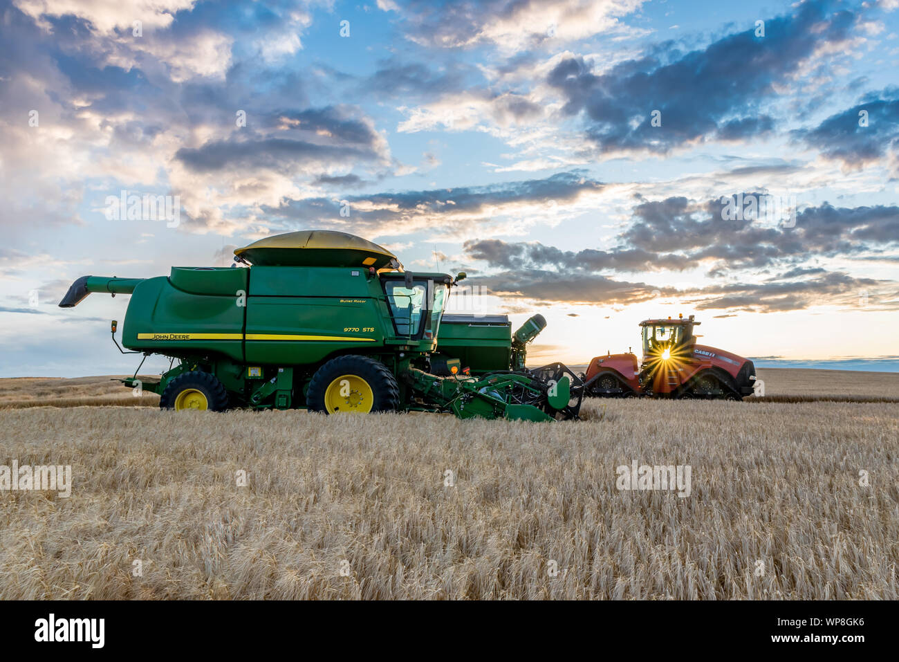 Swift Current, SK/Canada- Aug 25, 2019: Sunburst over combine and grain cart harvesting wheat in Saskatchewan Stock Photo