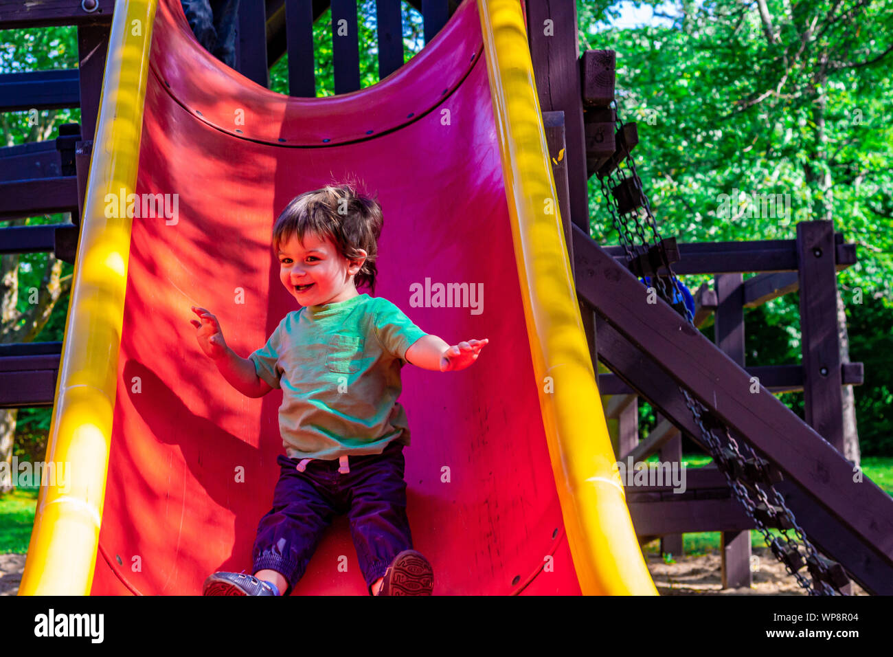 Young boy sliding down a slide in playground slide hires stock
