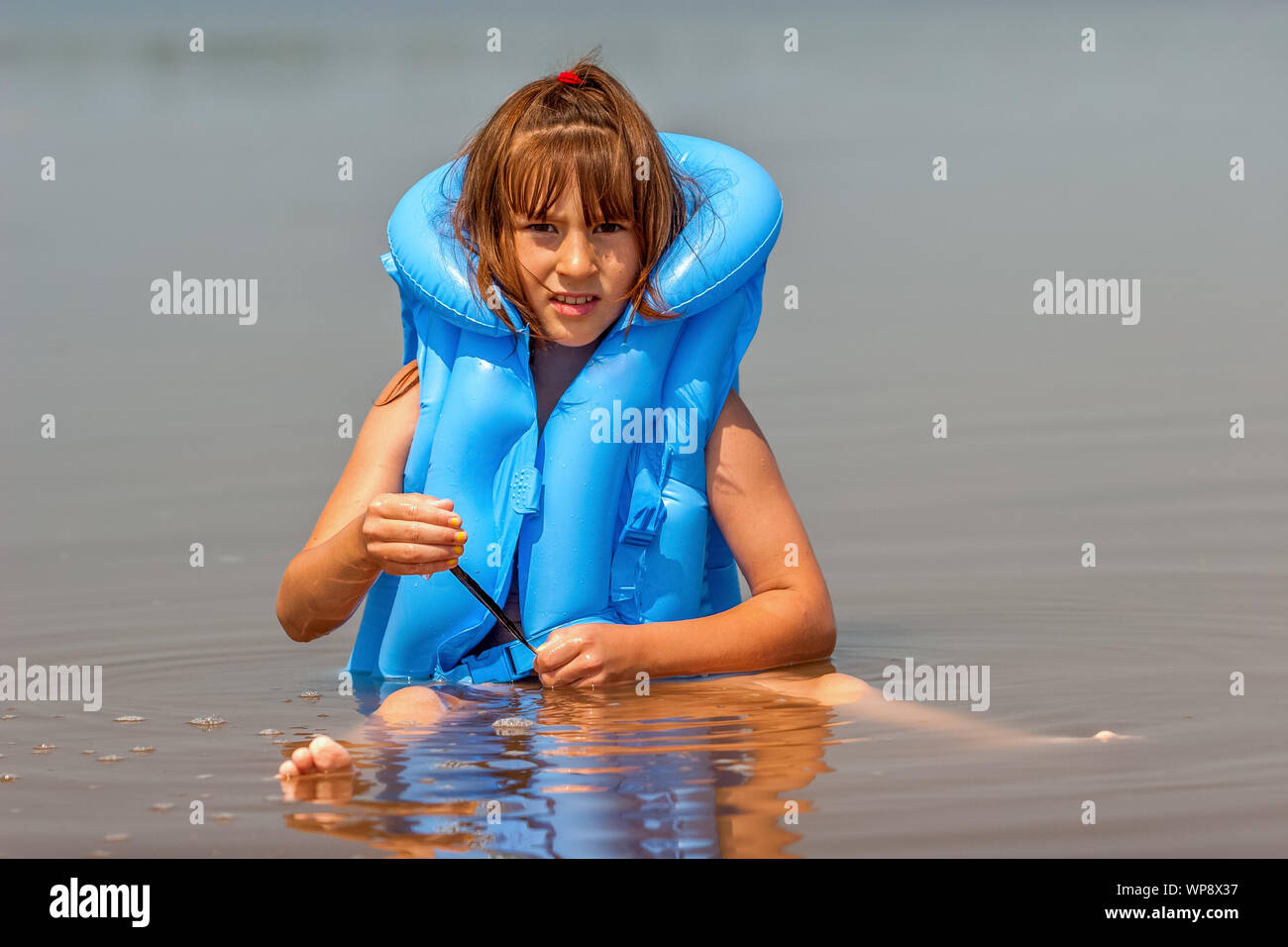 Child girl in a blue inflatable life jacket is played in the water with a  black