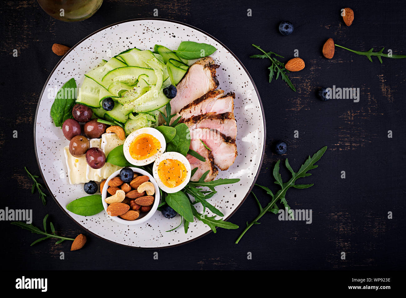 Ketogenic diet. Keto brunch. Boiled egg, pork steak and olives, cucumber, spinach, brie cheese