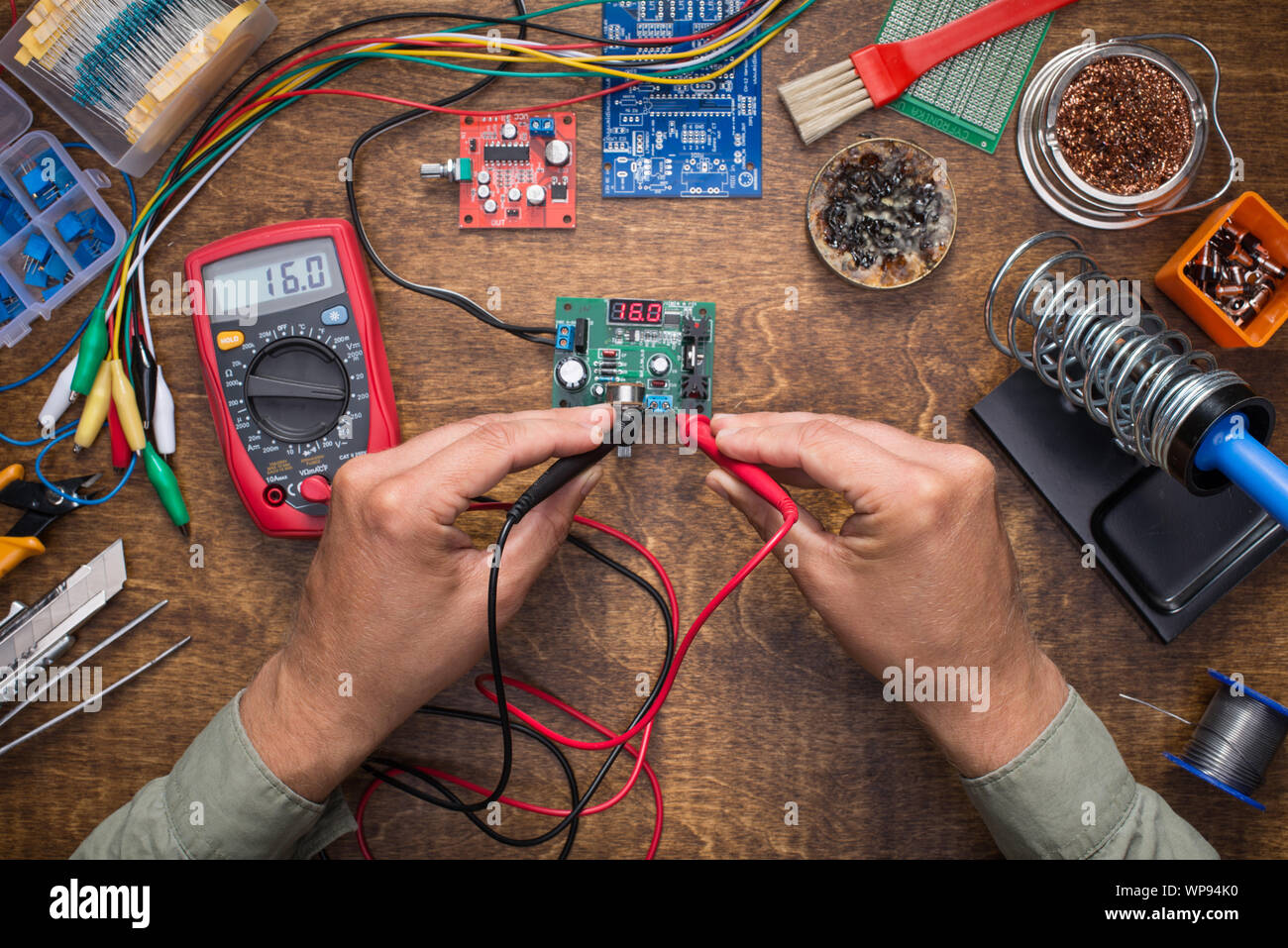 Hands measuring power supply voltage with tester. DIY, electronics, repair, making concept. Stock Photo
