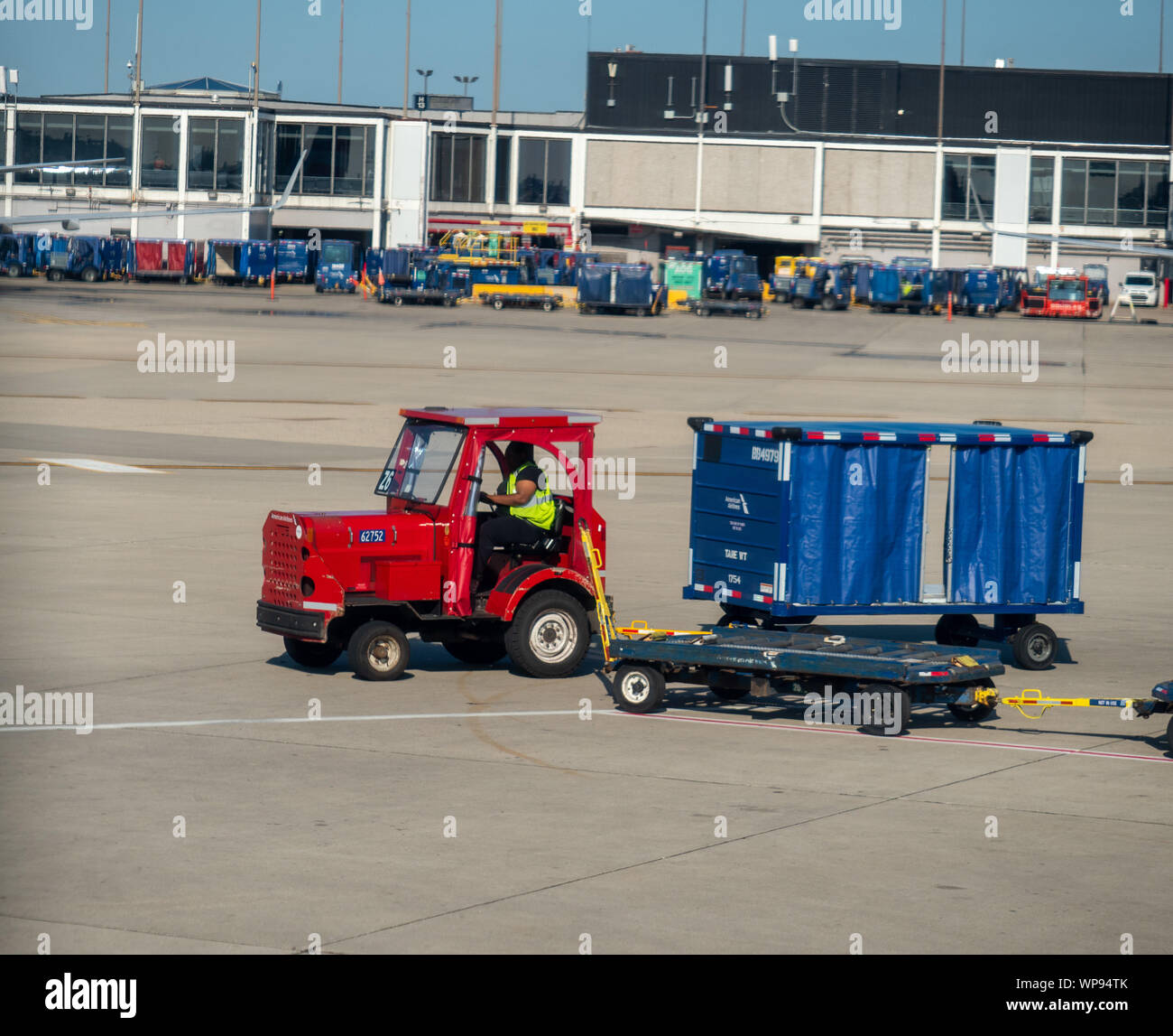 Man drives luggage truck on airport runway near terminal Stock Photo