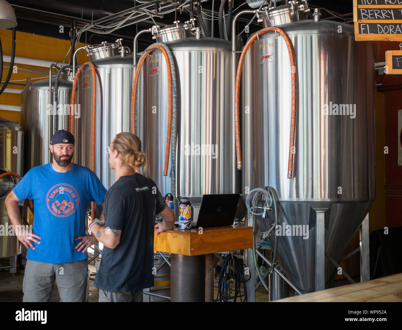 Two men talking in front of fermentation tanks at a brewery Stock Photo