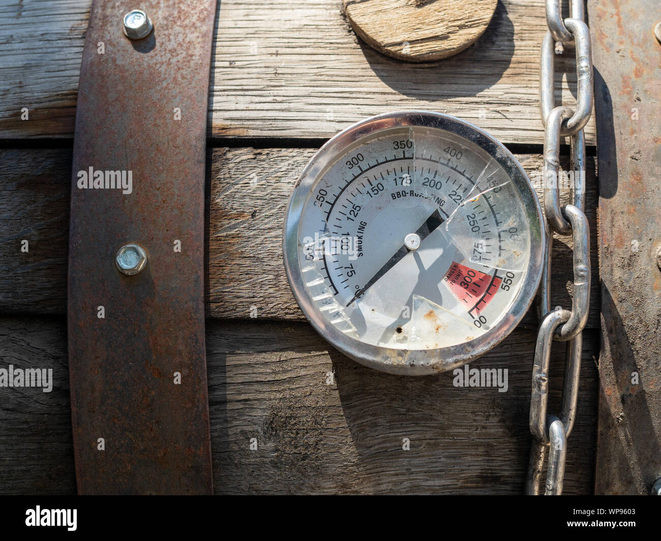 Broken thermometer gauge and chain sitting on top of smoker grill at 0 degrees Stock Photo