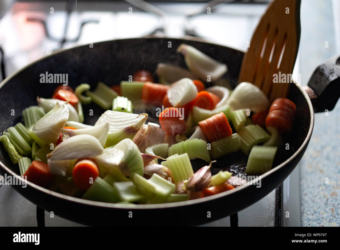 Frying onion, celery, garlic and carrots in pan with olive oil Stock Photo