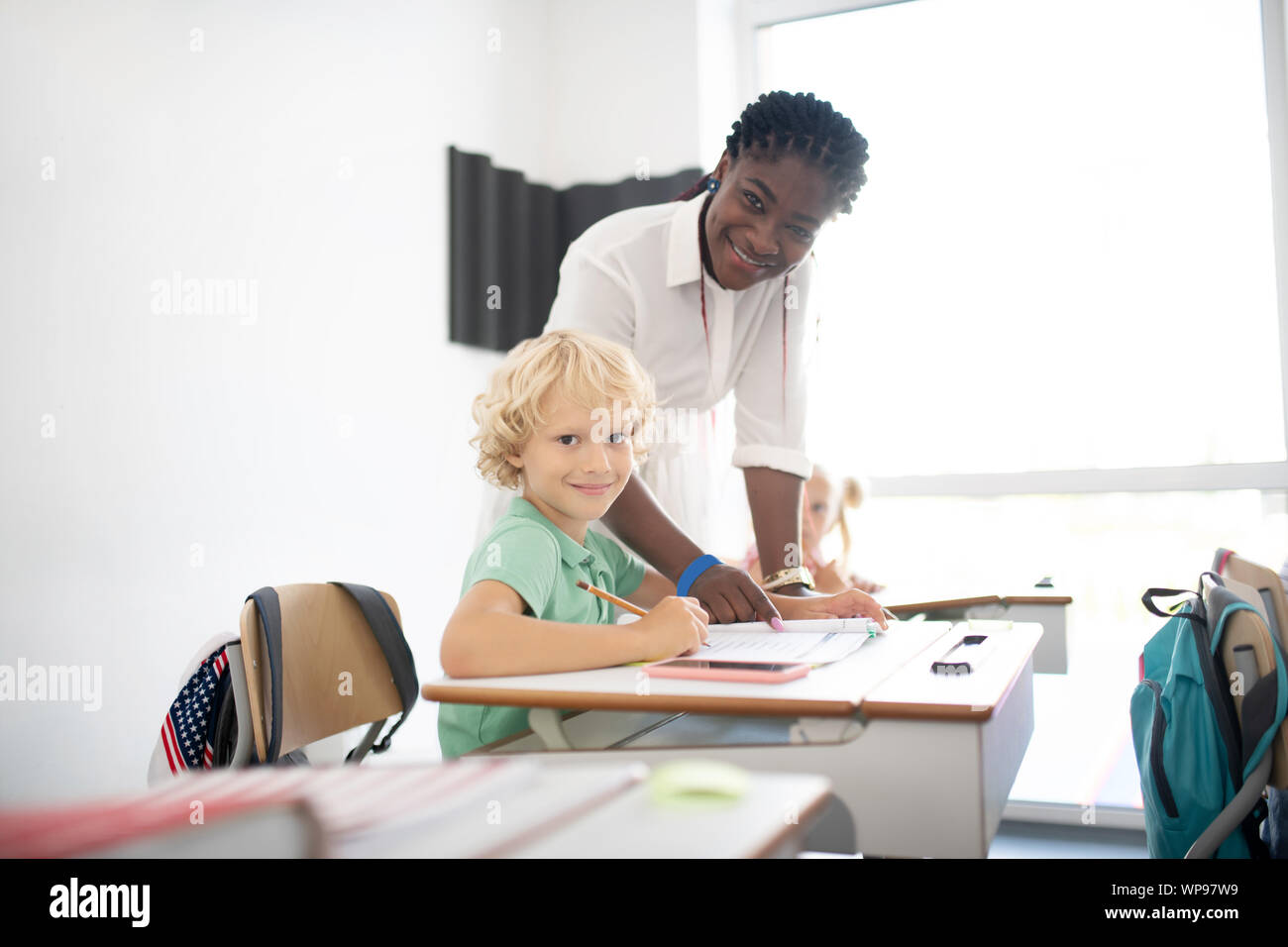 Pleasant dark-skinned teacher standing near pupil Stock Photo