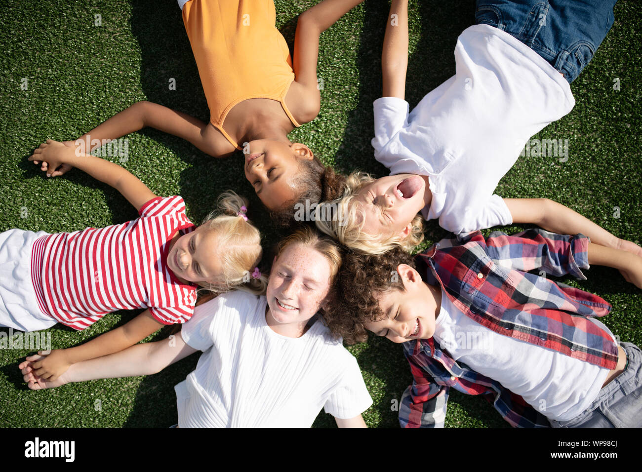 Children making funny faces while chilling on grass Stock Photo