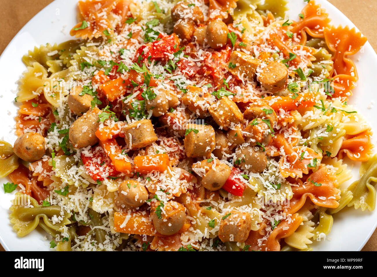 Farfalle pasta with sausages, vegetables and grated parmesan on plate - top view Stock Photo
