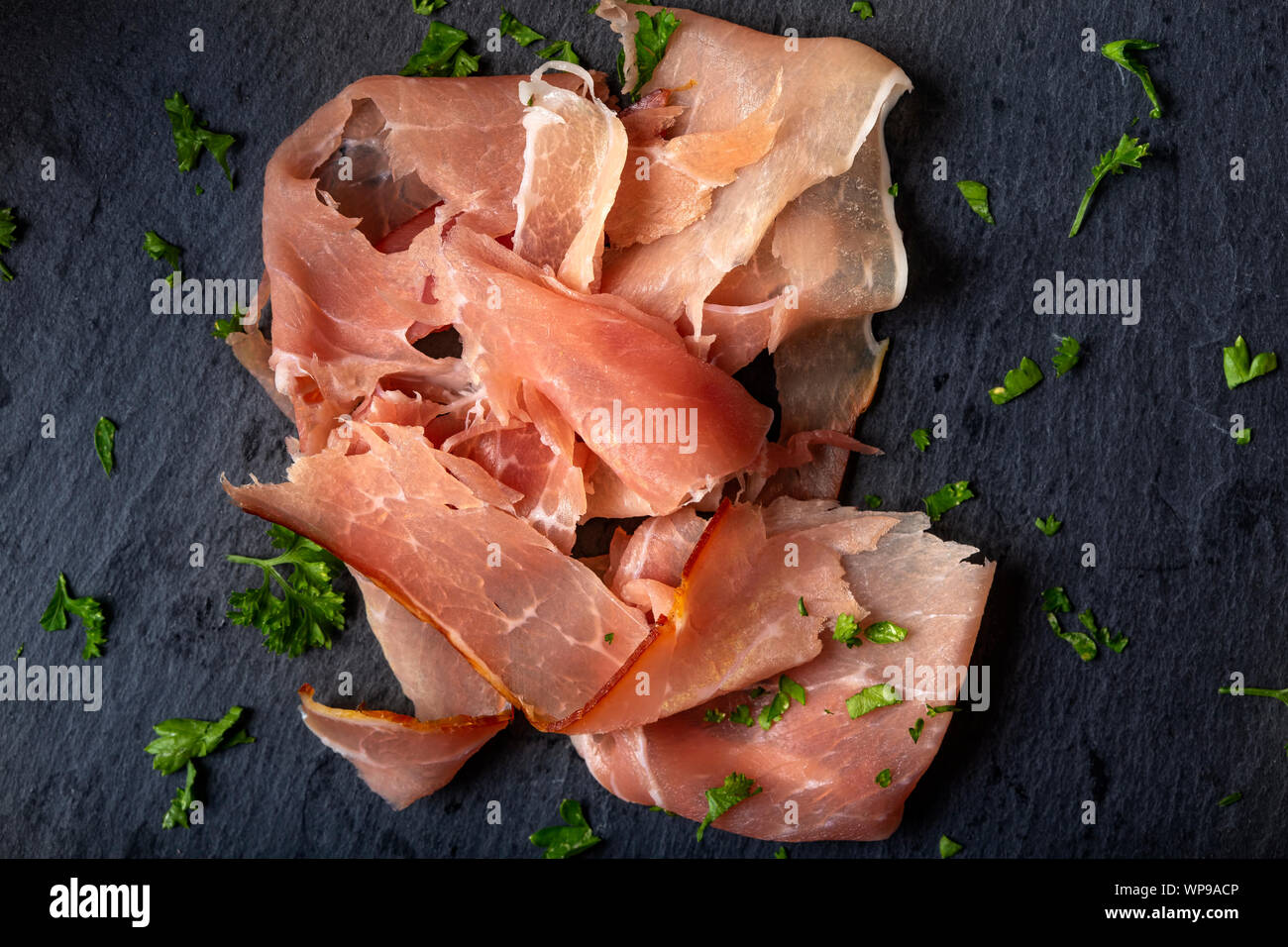 Thin sliced smoked pork ham on a dark slate with herbs - top view Stock Photo