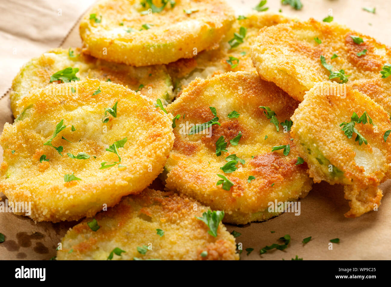 Fried slices of zucchini with green chopped parsley on paper Stock Photo