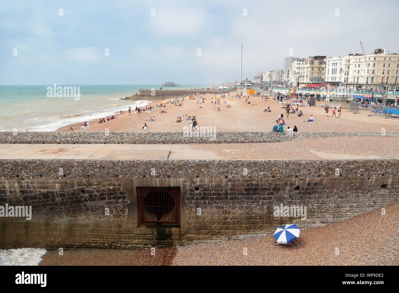 Solitary sun worshiper sits under their sunshade by a groyne outfall pipe on the famous Brighton Beach. Stock Photo