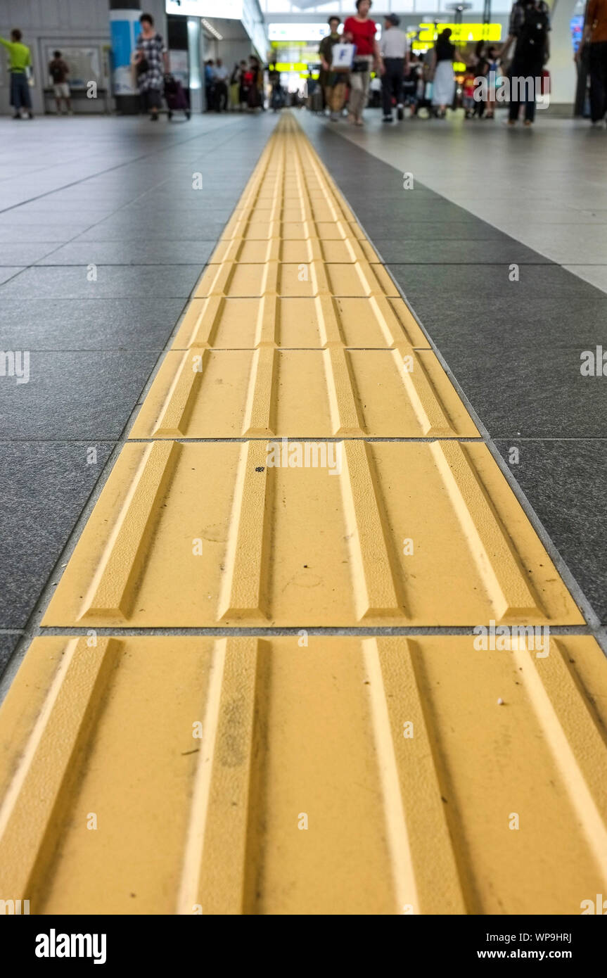 Yellow lines called “Tactile Ground Surface Indicators” (TGSI) or tenji blocks. In the Osaka Train Station, in Osaka Japan. Stock Photo