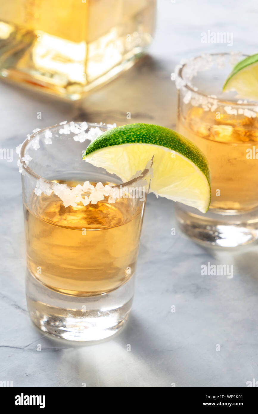 Golden tequila shots with lime slices, salt rim, and a bottle Stock