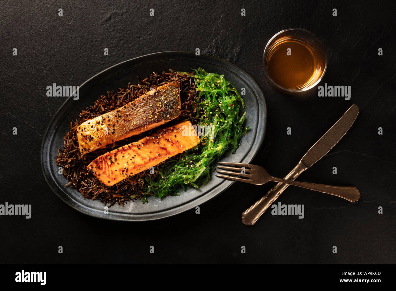 Salmon with sesame seeds, wakame seaweed and wild rice, shot from the top with a glass of white wine on a black background Stock Photo