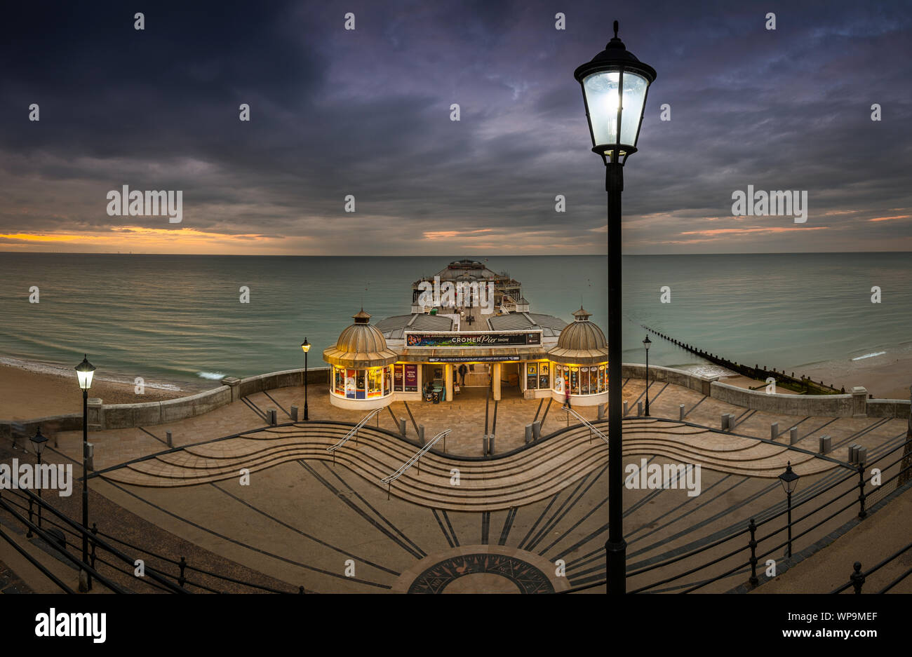 The street lights start to come on as the sun sets at Cromer pier. Stock Photo