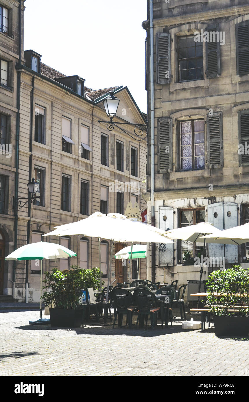 Geneva, Switzerland - July 19, 2019: Outdoor garden of cafe in historical city center. Traditional buildings. Vintage retro hipster style. French cafe, French-speaking Switzerland. Umbrella, chairs. Stock Photo