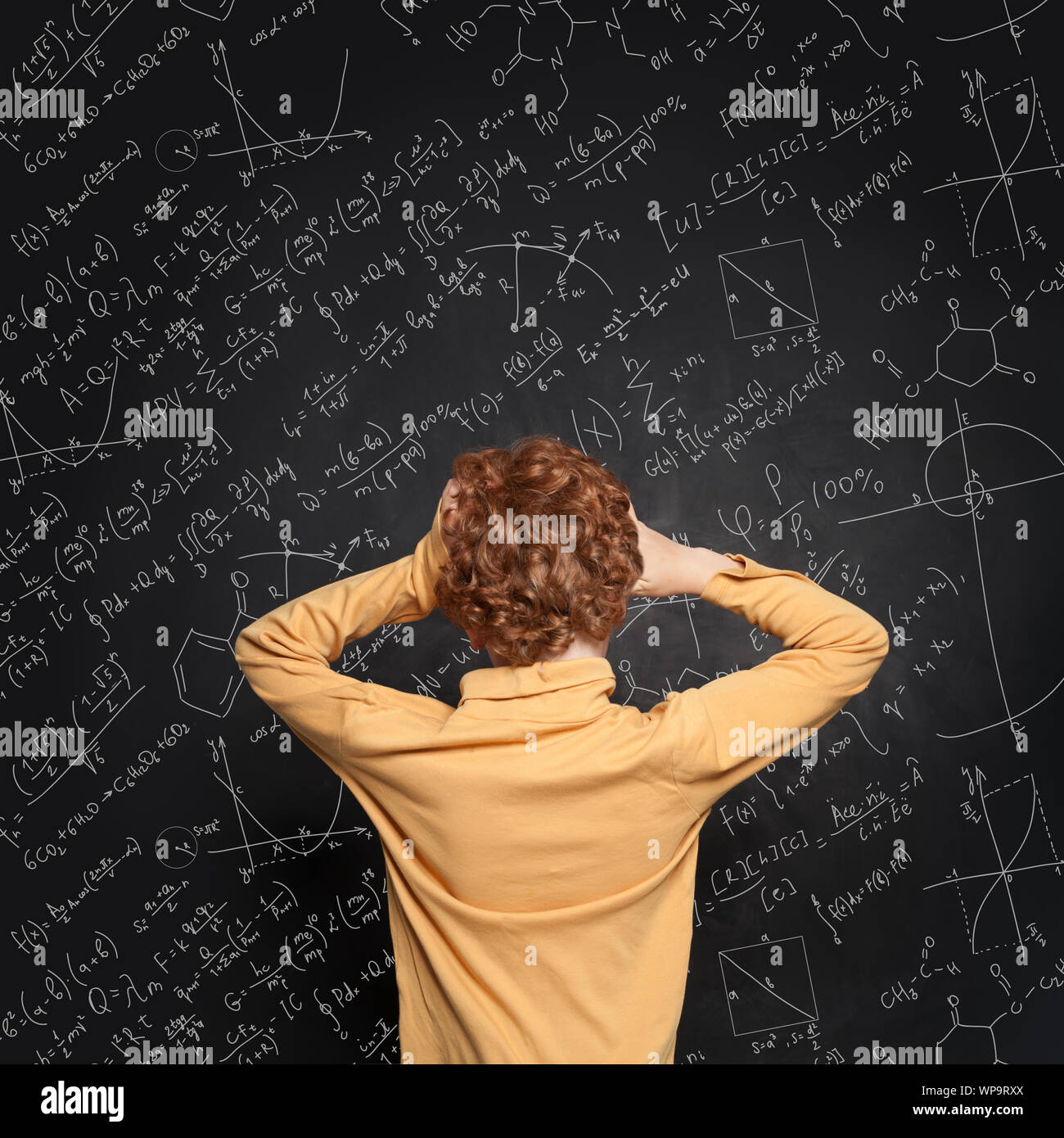Afraid child against blackboard background with science and maths formulas Stock Photo