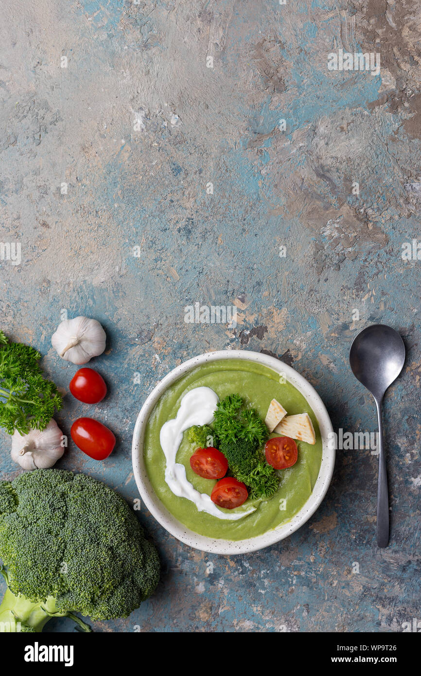 Cream soup with cream and broccoli and raw vegetables as tomatoes, garlic and parsley on blue background Stock Photo